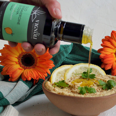 Vignoli Lemon Infused Extra Virgin Olive Oil front of 8.5oz bottle pouring over hummus