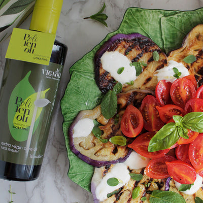 Coratina Monocultivar Extra Virgin Olive Oil front of 16.9oz bottle with grilled eggplant and fresh tomato and basil