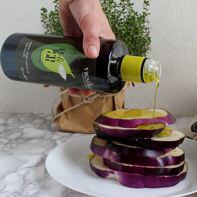 Coratina Monocultivar Extra Virgin Olive Oil front of 16.9oz bottle being poured over raw eggplant