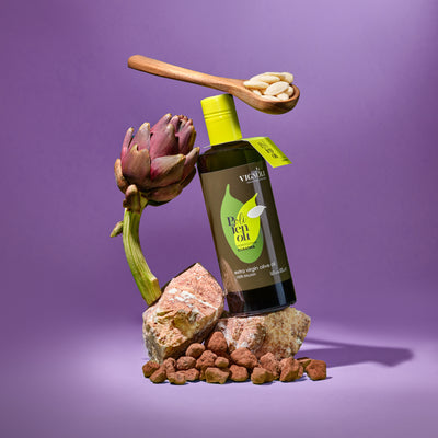 Coratina Monocultivar Extra Virgin Olive Oil front of 16.9oz bottle on rocks with artichoke and purple background