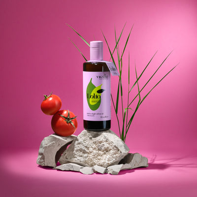 Biancolilla Monocultivar Extra Virgin Olive Oil front of 16.9fl oz bottle on rocks with tomato and pink background