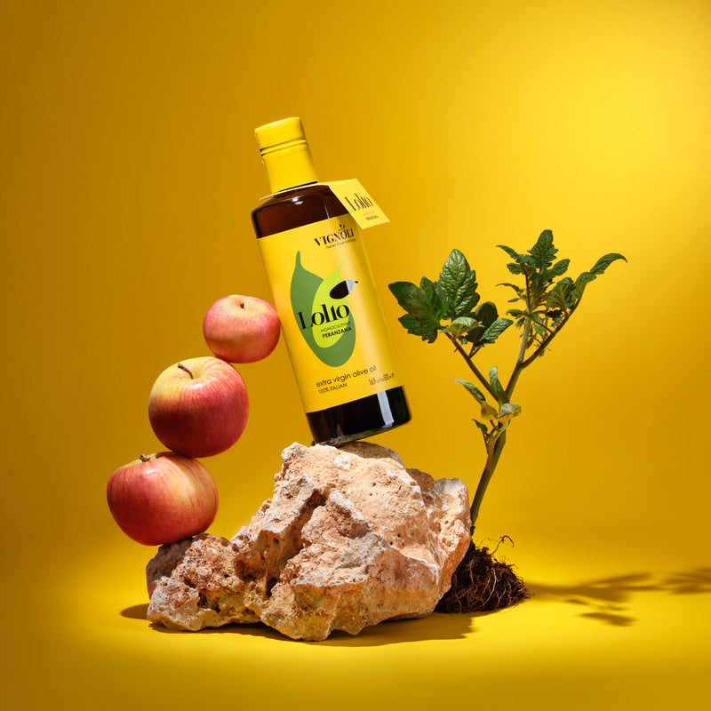Vignoli Peranzana Monocultivar Extra Virgin Olive Oil front of 16.9oz bottle on stone with apples