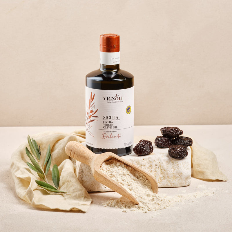 Vignoli Extra Virgin Olive Oil IGP Sicilia - Delicate front of 16.9oz bottle on white stone with raisins
