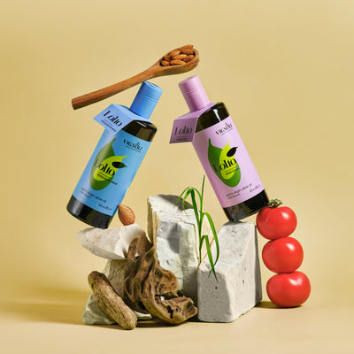 Vignoli Sicilian Lollo Monocultivar EVOO's Duo front 16.9oz bottles on rocks with tomatoes and wooden spoon with nuts