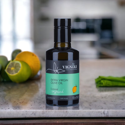 Vignoli Lemon Infused Extra Virgin Olive Oil front of 8.5oz bottle on table with lemon and lime in the background