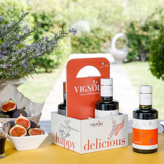 Vignoli SUMMER MEMORIES Serving Set with front view of 2 bottles of infused extra virgin olive oil and 2 bottles of infused balsamic vinegar Modena with garden in background