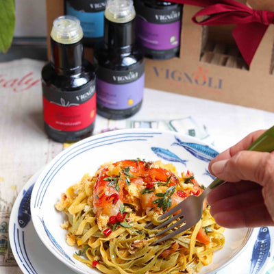 Blood Orange Infused Extra Virgin Olive Oil front of 8.5oz bottle on table with prawn pasta
