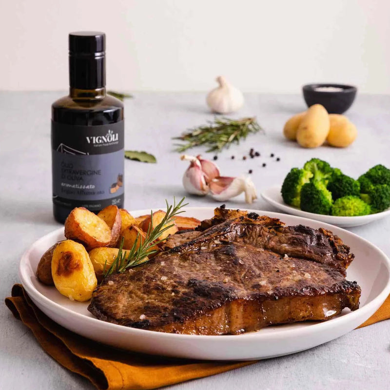 Vignoli Mesquite Smoked Infused Extra Virgin Olive Oil front of 8.5 oz bottle with steak and potatoes on kitchen counter